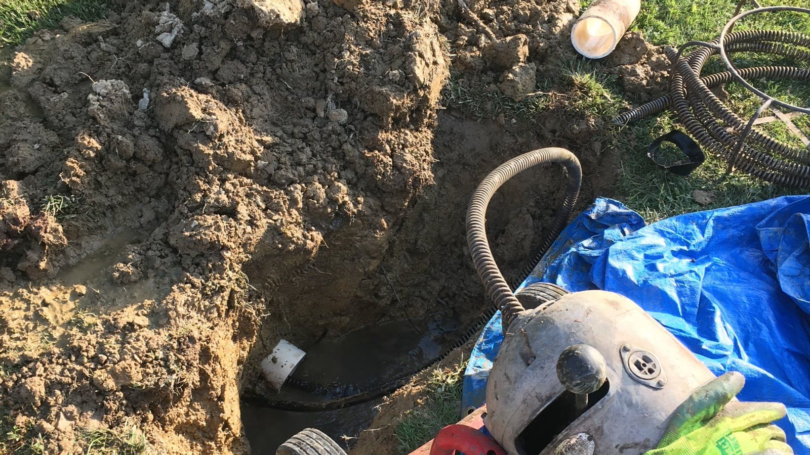 Technician using drain inspection equipment beside an open residential sewer-line access