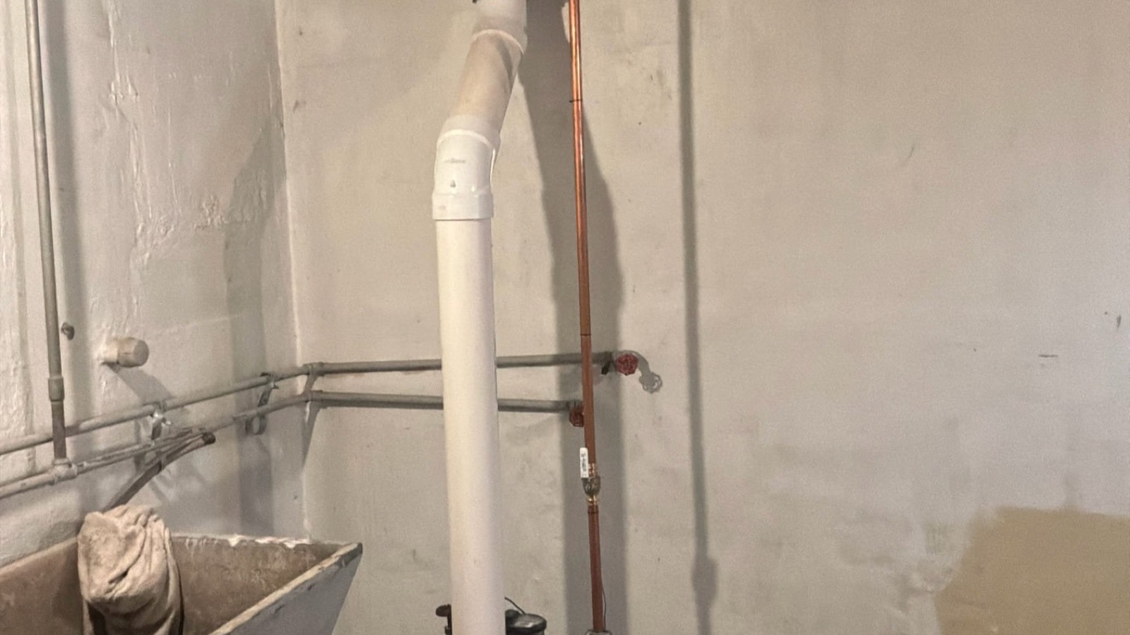 Exposed residential drain and water-supply lines in a basement utility area